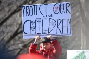 A boy perched atop a parent's set of shoulders holds up a sign calling on legislators to protect the children and speak up against guns. (Photo by Janelle Clausen)
