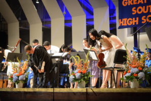 A student orchestra bows before a large crowd of cheering parents, friends and others. (Photo by Janelle Clausen)