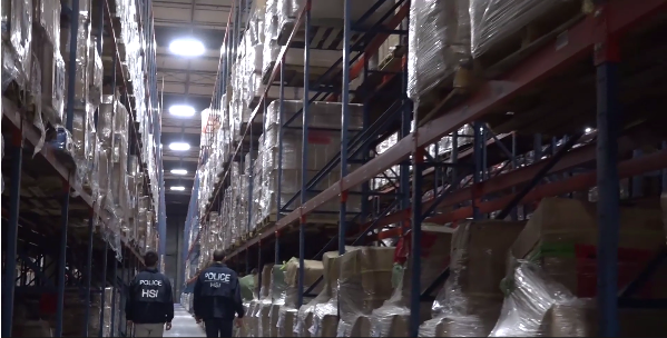 Two agents walk through a sea of seized counterfeit goods connected to the case. (Video still from U.S. Immigration and Customs Enforcement)